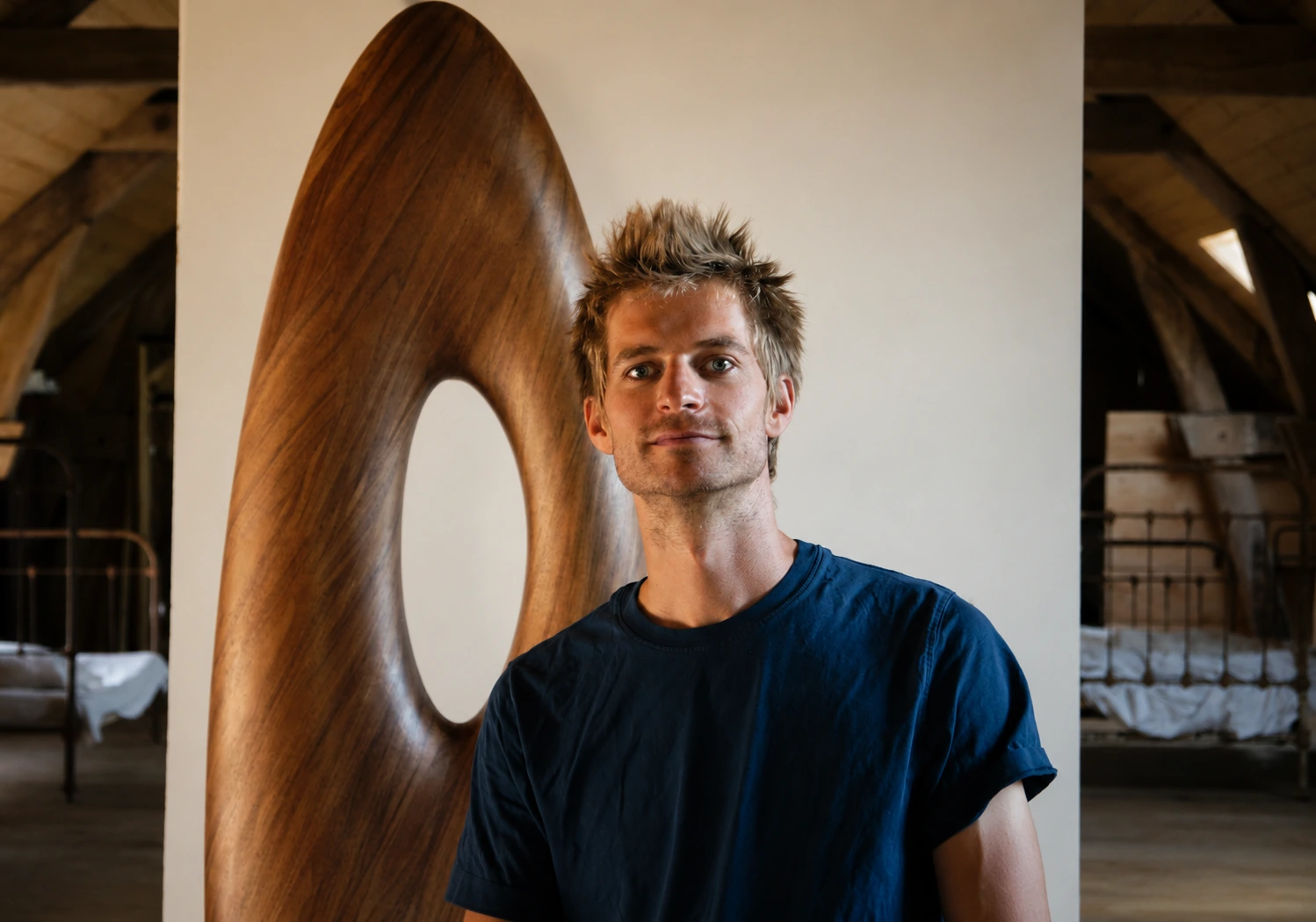Portrait beside a wooden sculpture beneath the roof structure.