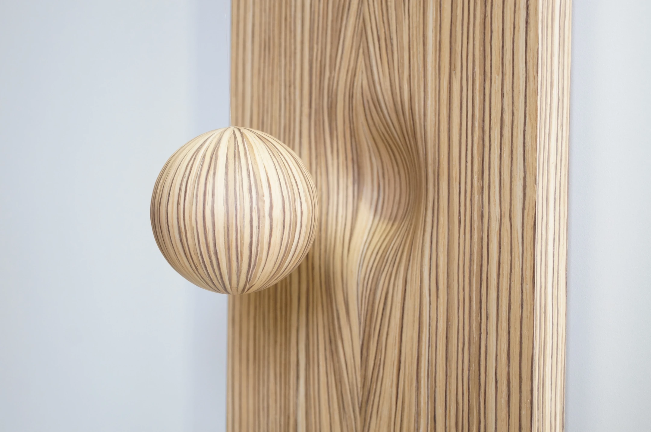A marquetry sphere with vertical grain in front of a curved panel with a matching pattern.